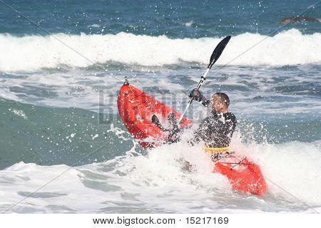 A strong athletic man kayaking in the sea with powerful waves.