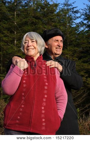 Senior couple embrace while enjoying a winter walk through a pine forest.