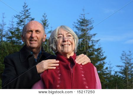 Senior couple embrace while enjoying a winter walk through a pine forest.