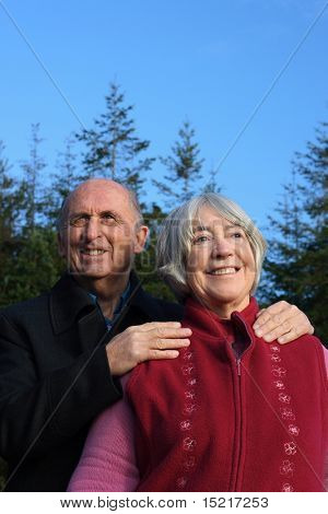 Senior couple embrace while enjoying a winter walk through a pine forest.