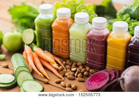 healthy eating, drinks, diet and detox concept - plastic bottles with different fruit or vegetable juices and food on wooden table