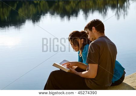 Couple Reading The Bible By A Lake