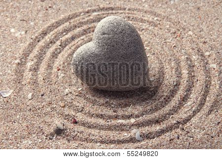 Grey zen stone in shape of heart, on sand background