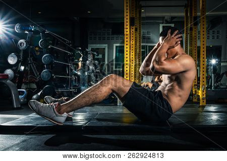 Muscular Guy Doing Sit Ups At Gym With Other People In Background. Young Athlete Doing Stomach Worko