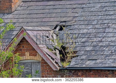 Damaged Slate Roof Tiles On A Pitched Roof On A Derelict House