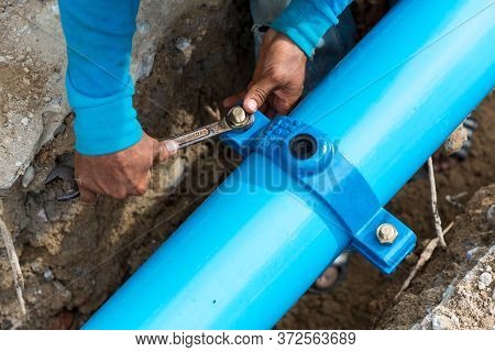 Man Using A Large Wrench On Water Pipes. Construction Site With New Water Pipes In The Ground. Sewer