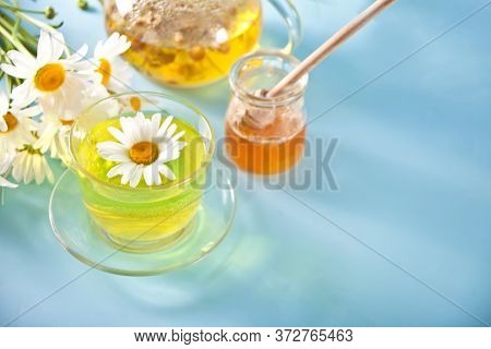 Glass Cup Of Healthy Herbal Camomille Tea With Camomille Flowers And Jar Of Honey On The Blue Backgr