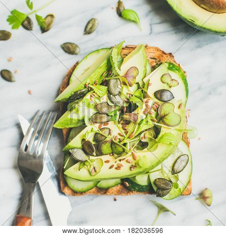 Healthy green veggie breakfast concept. Sandwich with avocado, cucumber, kale, kress sprouts, pumpkin seeds over marble background, top view, square crop. Vegan, weight loss, detox, diet food concept