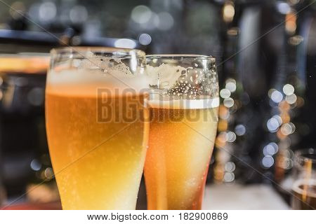 Light beer in a beer glass and dark beer in a small glass lighted with warm light close up