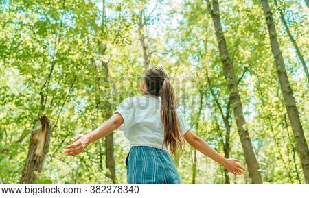 Free woman breathing clean air in nature forest. Happy girl from the back with open arms in happiness. Fresh outdoor woods, wellness healthy lifestyle concept.