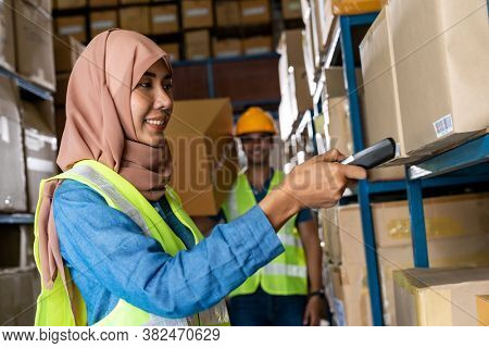 Asian Islam Muslim female warehouse worker do inventory with barcode scanner with Indian worker hold cardboard box in warehouse distribution. For business warehouse inventory and logistic concept.