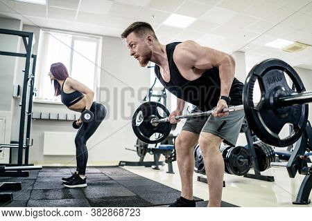 Sport, Bodybuilding, Lifestyle And People Concept - Young Man And Woman With Barbell Flexing Muscles