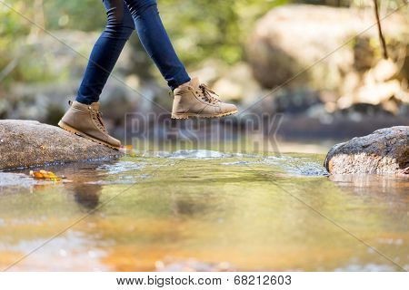 young woman hiking in mountain crossing stream