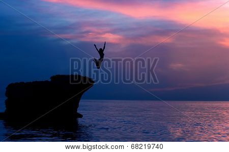 Brave girl jumping from the rocks in the evening on beautiful purple sunset background, summer adventure, freedom concept