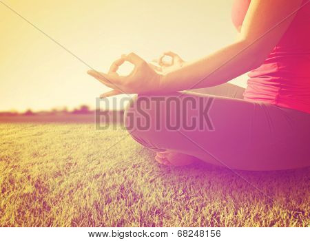  hands of a woman meditating in a yoga pose on the grass toned with a soft instagram like filter