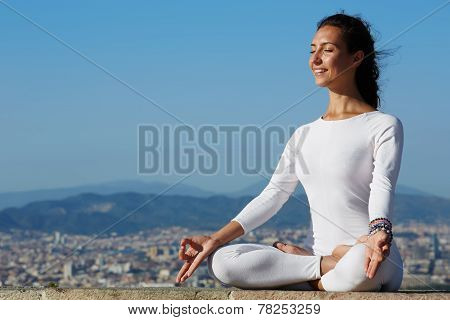 Yoga on high altitude with big city on background smiling woman seated in yoga pose