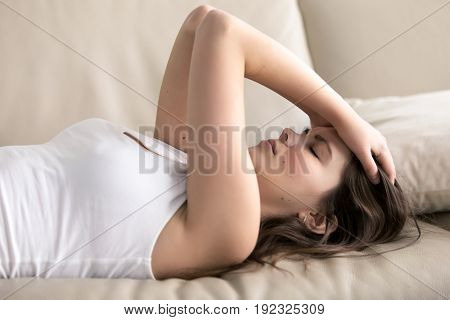 Woman lying on sofa having headache. Stressed girl suffering of fatigue, migraine, trying to cope with nervous tension, worries because of problems, unwanted pregnancy, negative thoughts and emotions