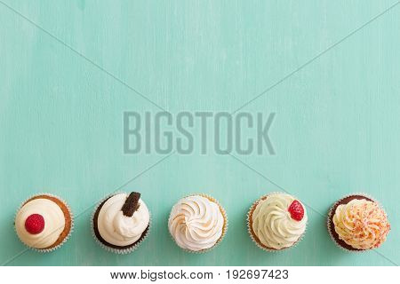 Top view on homemade vanilla blueberyy lemon chocolate cupcakes in row on turquoise retro wooden background. Healthy food snack for birthday party or celebration