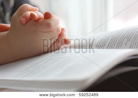 Young Child's Hands Praying On Holy Bible