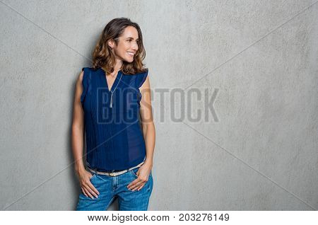 Happy smiling woman dressed in a blue dress isolated on grey background. Mature woman looking away against grey background. Beautiful woman in casual thinking with copy space.