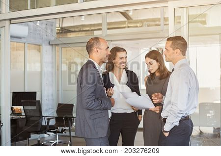 Company employees in conversation regarding paperwork in meeting room. Manager and businessman with businesswomen working together in modern office. Conversation with colleagues in modern office.