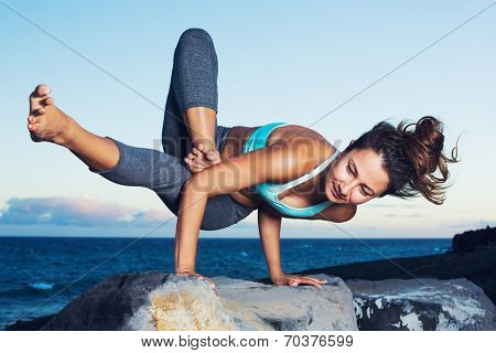 Athletic strong woman practicing difficult yoga pose outdoors