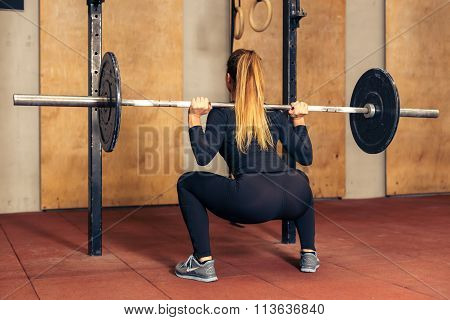 Back view girl doing heavy squat with barbell