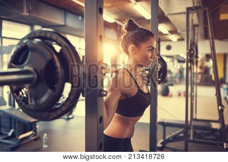 Fit beautiful girl doing squats with barbell in gym