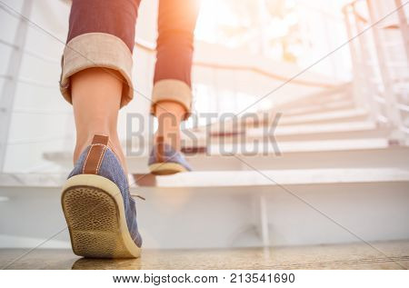 Young adult woman walking up the stairs with sun sport background.