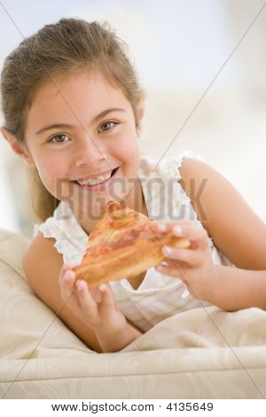 Young Girl Eating Pizza Slice In Living Room Smiling