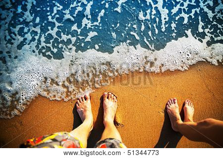 Male and female feet are standing on the sandy beach