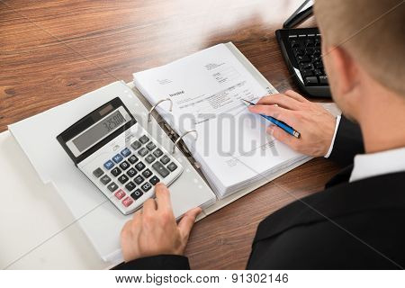 Businessman Calculating Invoice At Desk In Office