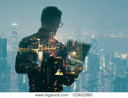 Double exposure young bearded businessman wearing black shirt and holding modern notebook hands. Panoramic view contemporary night city background.