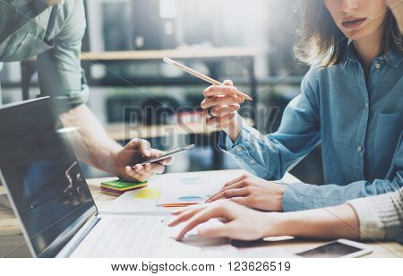 Coworking process. Photo young business crew working with new startup project. Notebook on wood table.  Woman showing screen laptop, man holding smartphone. Blurred background, film effect.