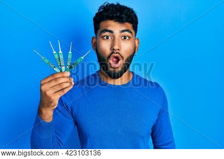 Arab man with beard holding picklock to unlock security door scared and amazed with open mouth for surprise, disbelief face 