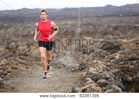 Trail runner - running man trail runner cross country training outdoors for marathon or triathlon. Male athlete working out on Hawaii, Big Island, USA. Triathlete listening to music on smart phone