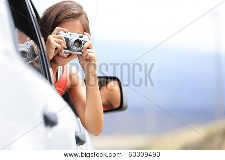 Woman tourist taking photo in car with camera driving on road trip travel vacation. Girl passenger taking picture out of window with vintage retro camera.