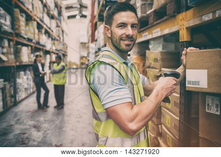 Warehouse worker scanning box while smiling at camera in a large warehouse