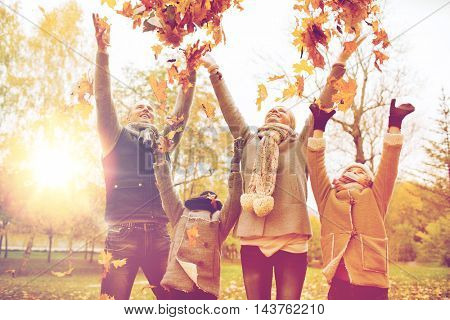 family, childhood, season and people concept - happy family playing with autumn leaves in park