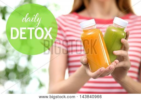 Woman holding bottles with delicious detox drinks. Text daily detox on blurred background. Detox diet concept.