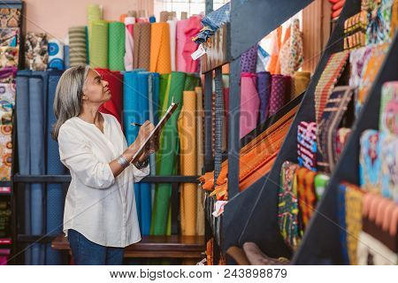 Mature Fabric Store Owner Standing In Her Shop Surrounded By Colorful Cloths And Textiles Taking Inv