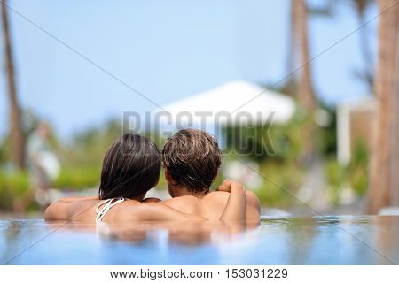 Honeymoon couple relaxing together in an infinity swimming pool in luxury resort spa retreat beach destination. Luxurious hotel travel vacation. Unrecognizable people relaxed enjoying summer holidays.