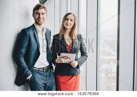 Group of business people a man in a suit and a woman in a red dress and jacket holding a tablet winter city landscape outside the window on the background