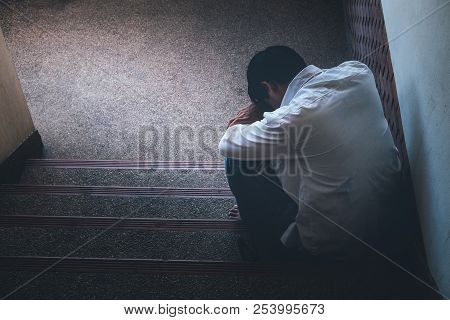 Depressed Man Sitting Head In Hands On The Stairs In Building. With Low Light Environment, Dramatic