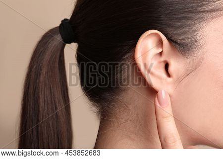 Young Woman Pointing At Her Ear On Beige Background, Closeup