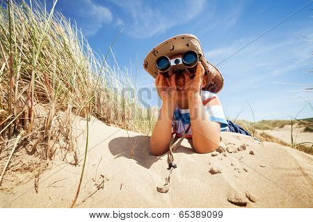 Little boy searching with binoculars at the beach dressed as explorer concept for nature, discovery, exploring and education