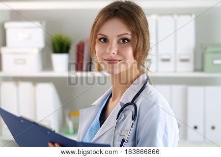 Smiling female medicine doctor filling in patient medical history list during ward round. Medical care or insurance concept. Physician ready to examine patient and help.