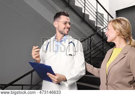 Happy Doctor With Clipboard And Patient In Clinic