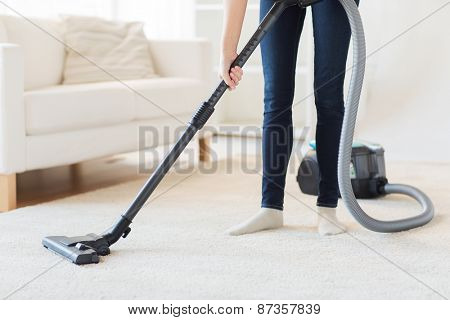 people, housework and housekeeping concept - close up of woman with legs vacuum cleaner cleaning carpet at home