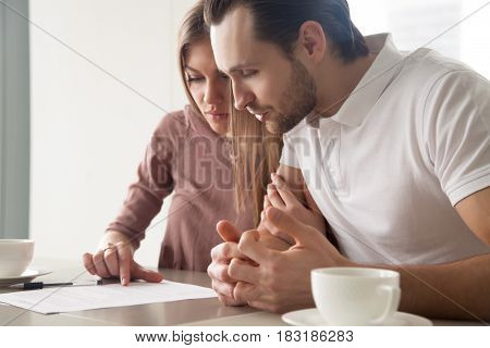 Serious couple studying contract agreement, reading terms and conditions attentively before signing, husband and wife calculating domestic bills, considering mortgage loan offer, health insurance